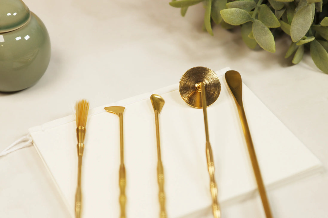 Five brass incense sealing tools laid out on white surface including lotus stamp, brush, spade, spoon and scoop