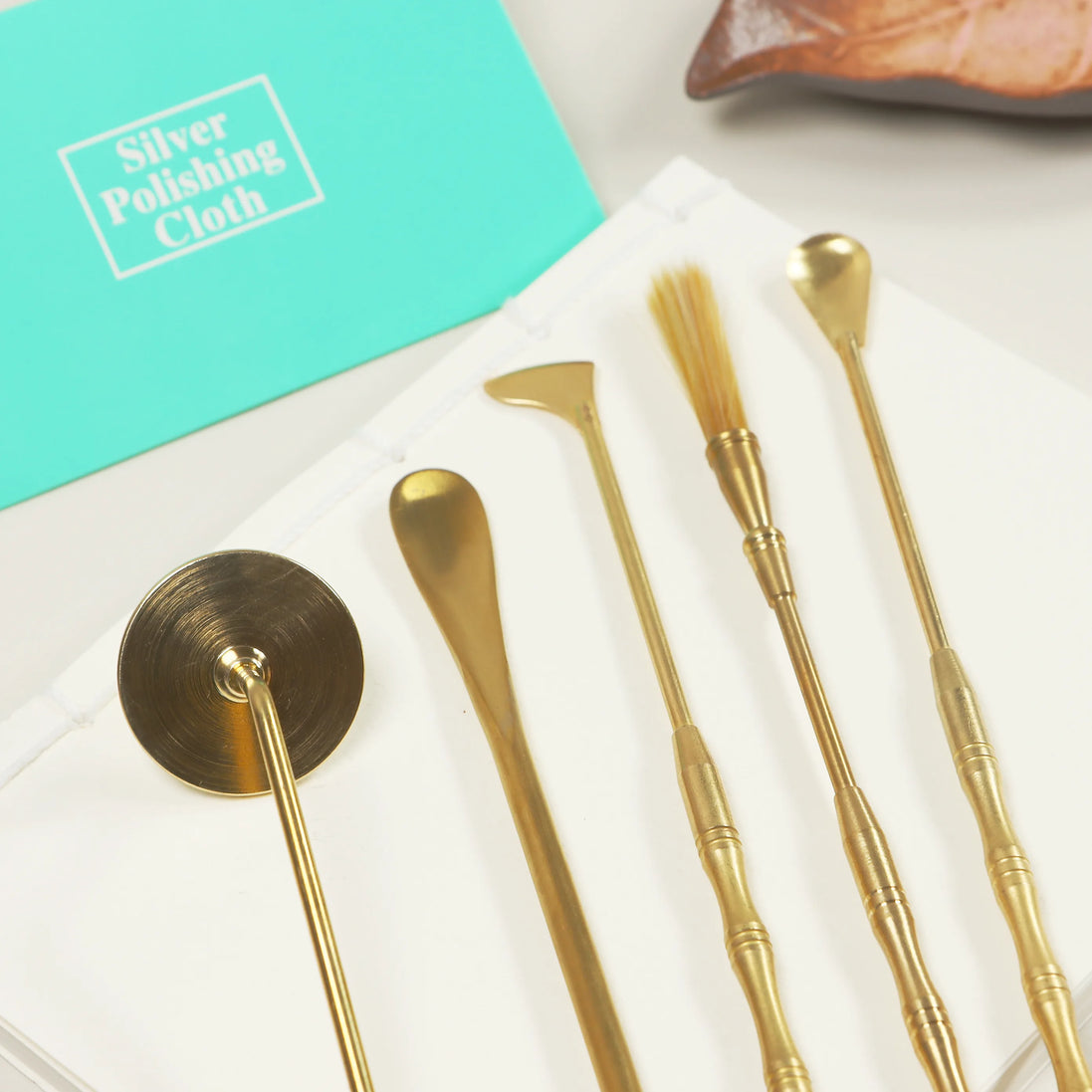 Mint green silver polishing cloth package next to golden brass tools on white marble surface