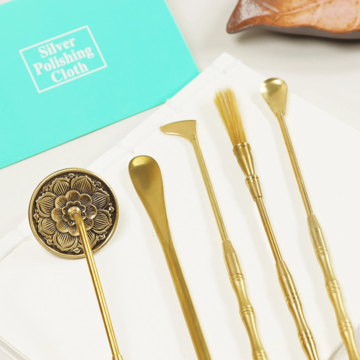 Golden brass skincare tools with ornate floral design alongside turquoise silver polishing cloth on white marble