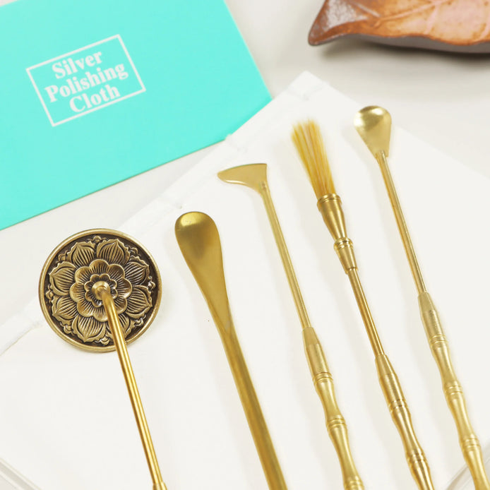 Golden brass skincare tools with ornate floral design alongside turquoise silver polishing cloth on white marble