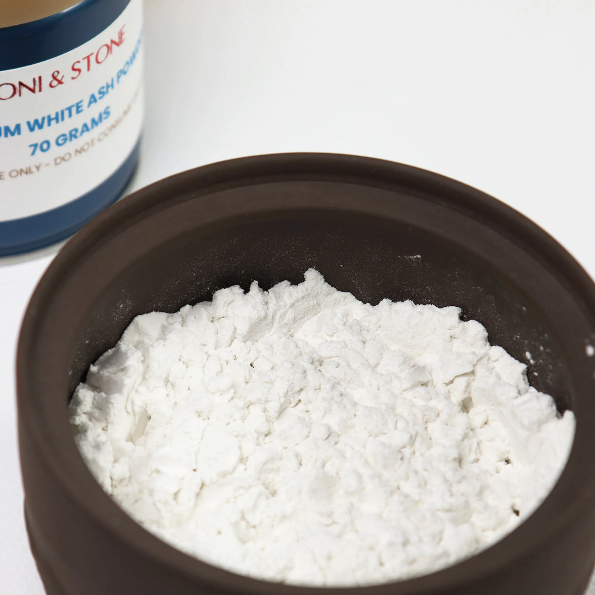 Fine white ash powder in dark bowl with Peoni & Stone container showing 70 gram package