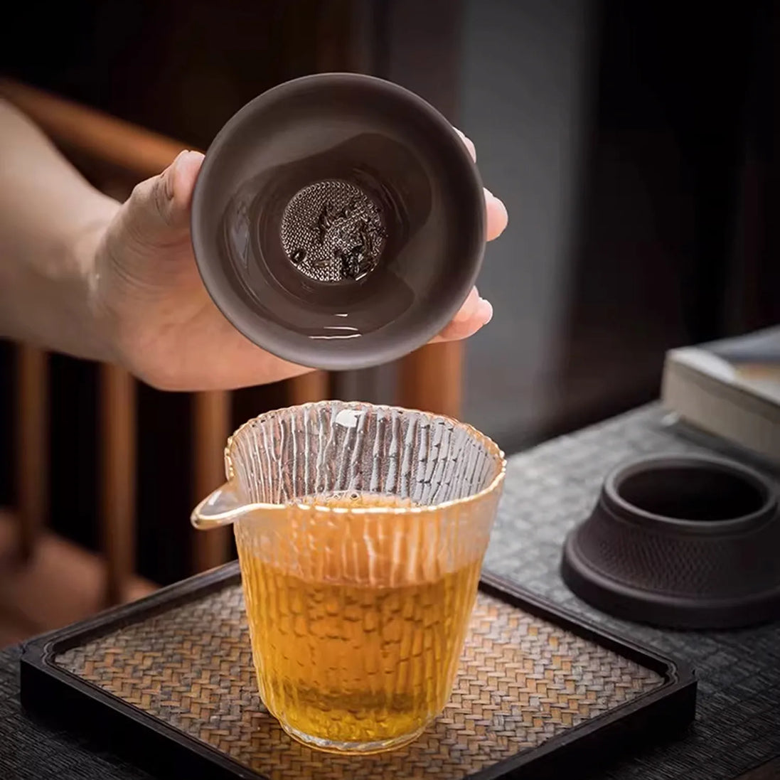 Purple clay tea strainer with mesh filter held over glass cup brewing golden tea