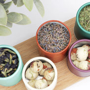 Colourful travel containers with loose leaf tea and bath bombs on wooden board