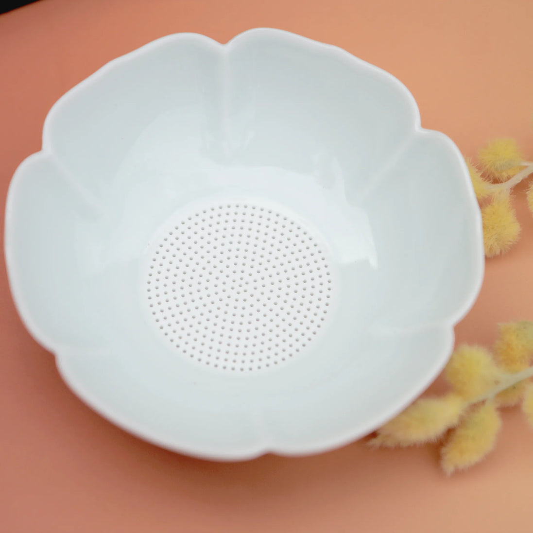 White flower-shaped ceramic tea strainer with fine mesh centre on peach background