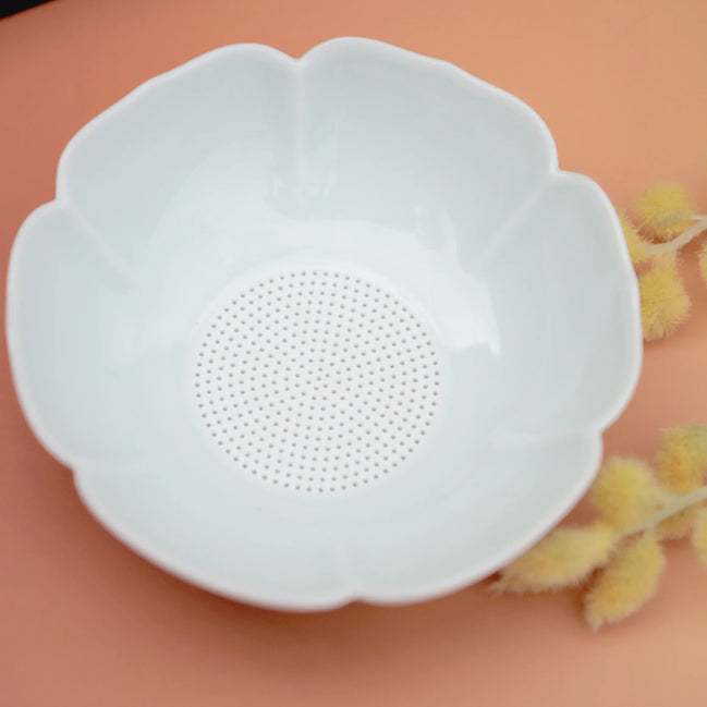White flower-shaped ceramic tea strainer with fine mesh centre on peach background