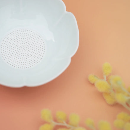 White flower-shaped tea strainer with fine mesh on coral background with yellow dried flowers