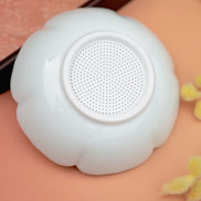 White flower-shaped tea strainer with fine mesh centre on peachy pink background