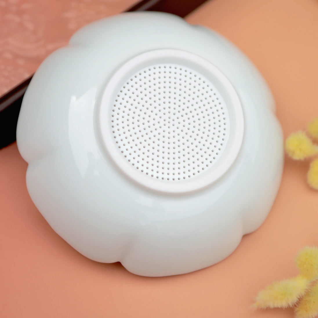 White flower-shaped tea strainer with fine mesh centre on peachy pink background